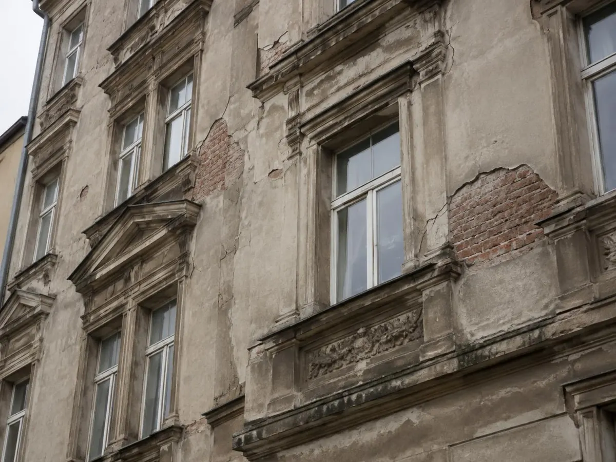 Altbaufassade mit abgeplatztem Putz, freiliegendem Ziegelmauerwerk und Rissen an Fensterecken